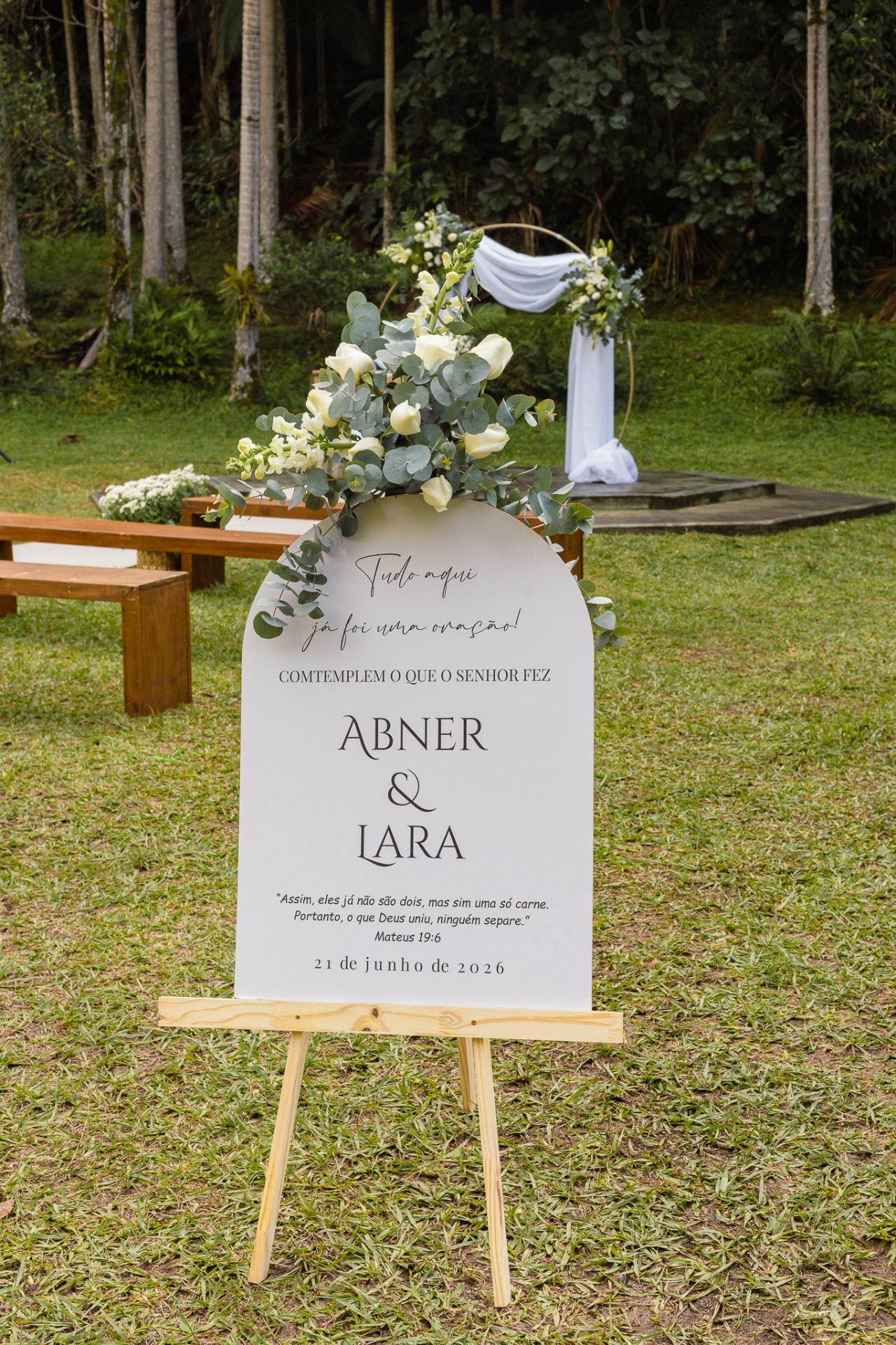 Placa de boas-vindas do casamento com arranjo de eucalipto e rosas brancas na entrada da cerimônia