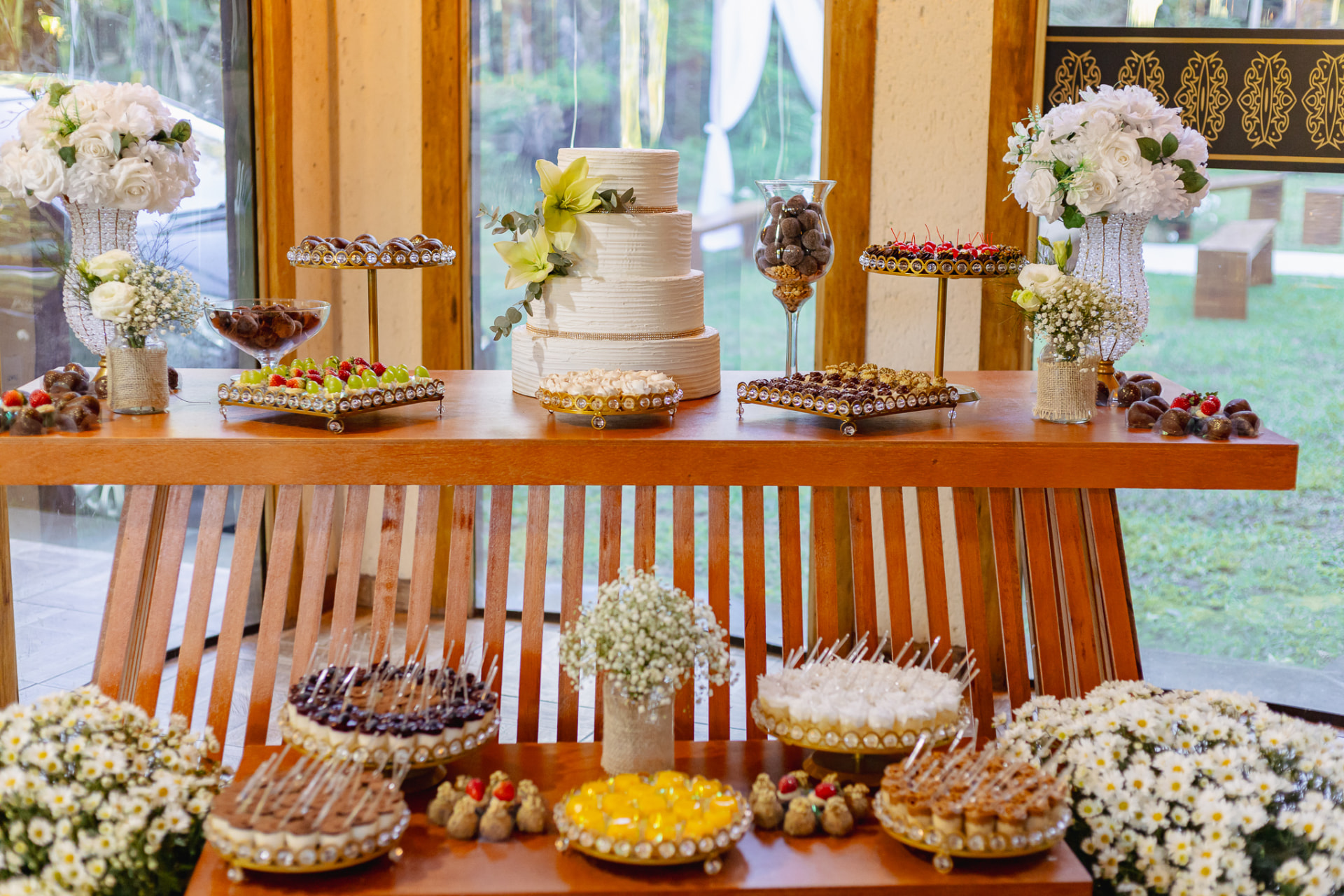 Mesa do bolo de casamento com doces finos, arranjos de flores brancas e decoração elegante