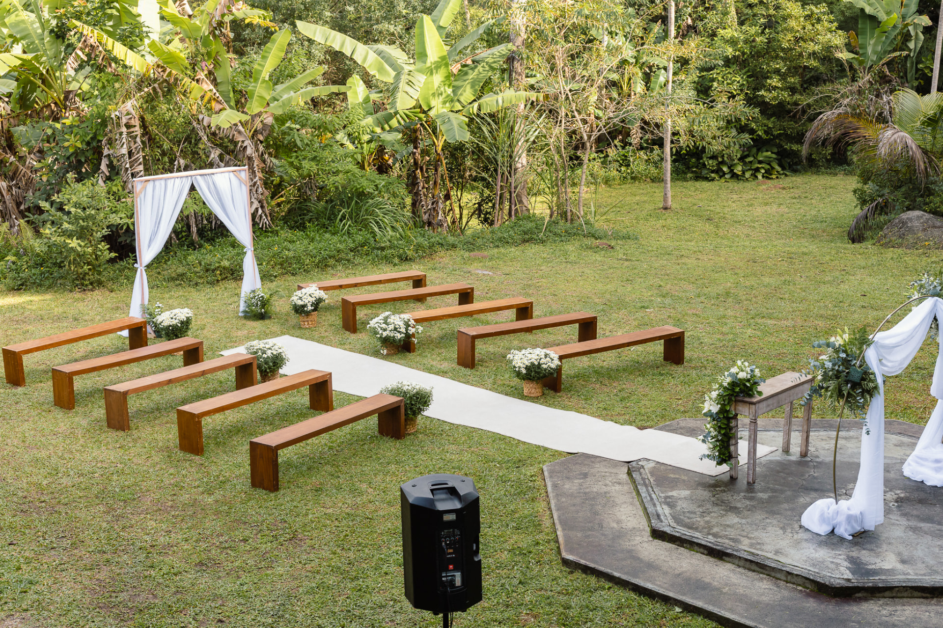 Cerimônia de casamento ao ar livre com bancos de madeira, passadeira branca e decoração floral no campo