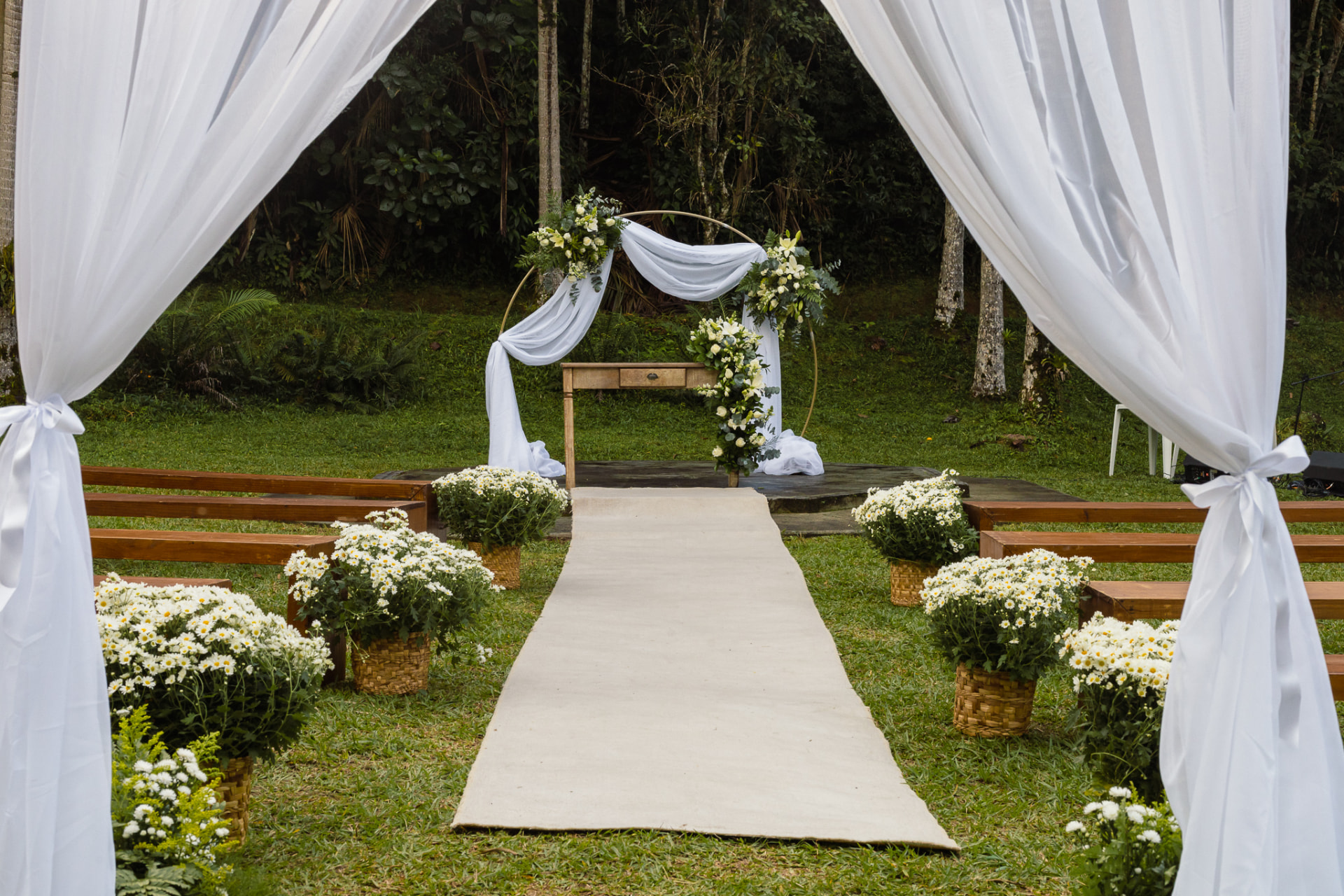 Cerimônia de casamento ao ar livre com arco floral, passadeira e bancos de madeira em meio à natureza